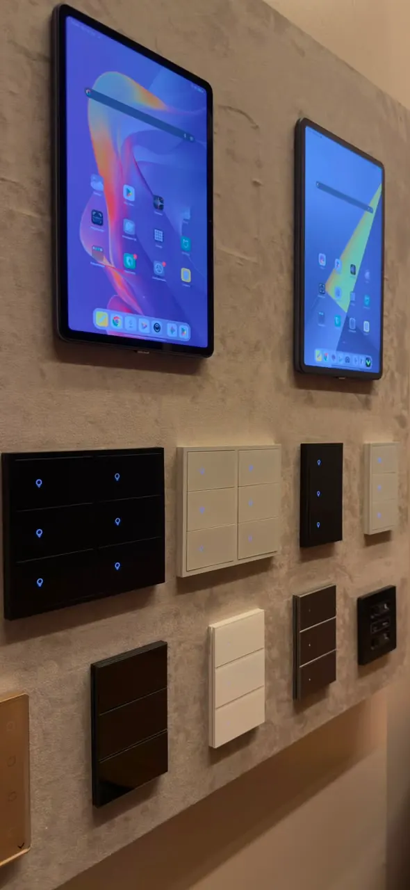 Parede de mostruário com dois tablets e teclados de cena em vários acabamentos: preto, branco, bege e grafite.